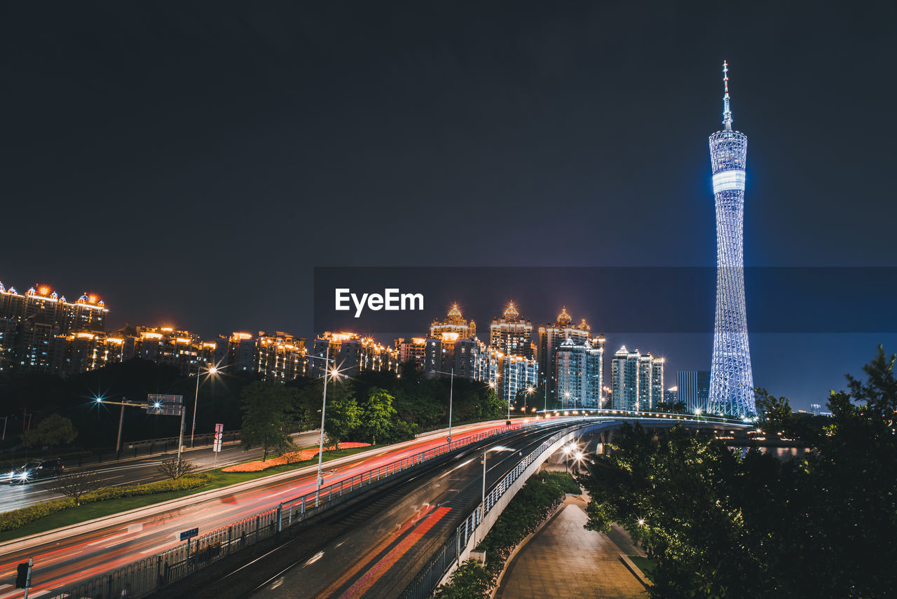 LIGHT TRAILS ON ROAD AMIDST BUILDINGS AGAINST SKY