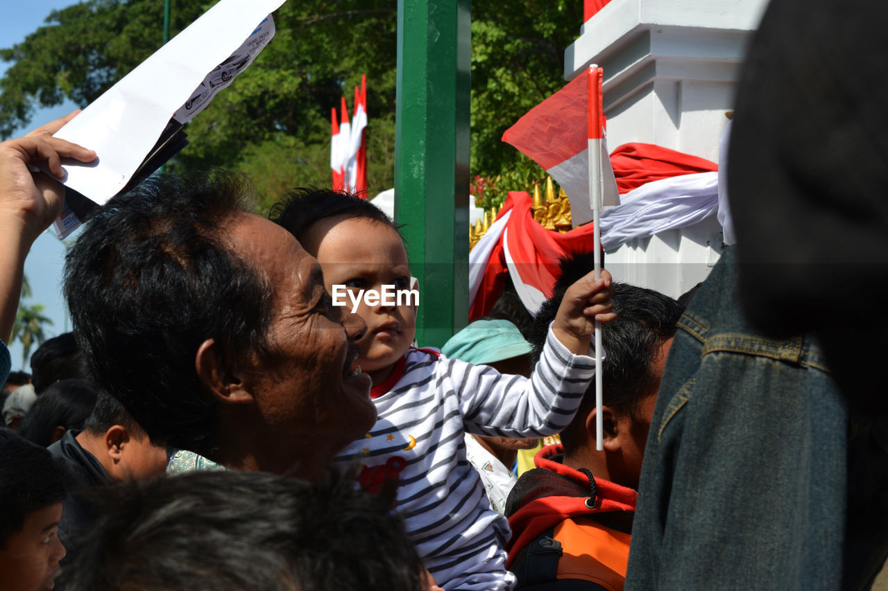 REAR VIEW OF PEOPLE STANDING AGAINST FLAG