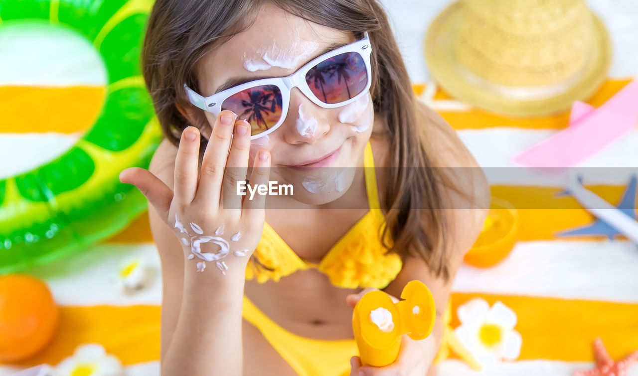 Happy girl wearing sunglasses applying suntan lotion