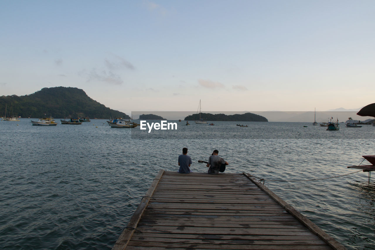 PEOPLE ON PIER AMIDST SEA AGAINST SKY