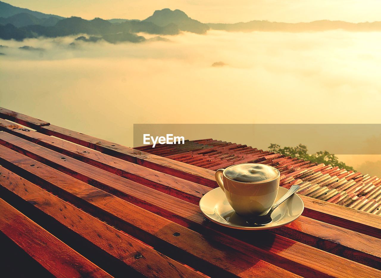 COFFEE CUP ON TABLE AGAINST SKY AT SUNSET