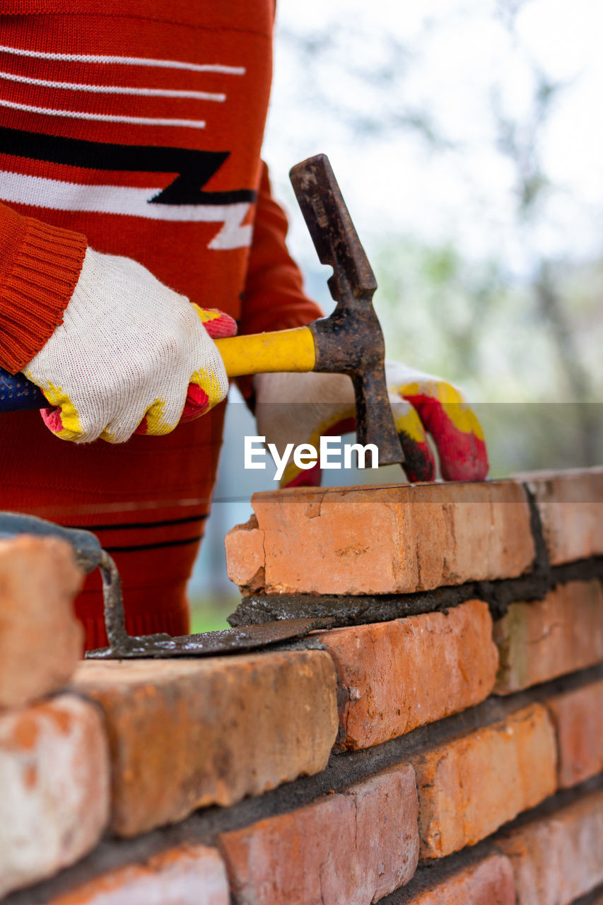 A man builds a brick wall, puts a brick on a cement-sand mortar, tapping a brick with a hammer