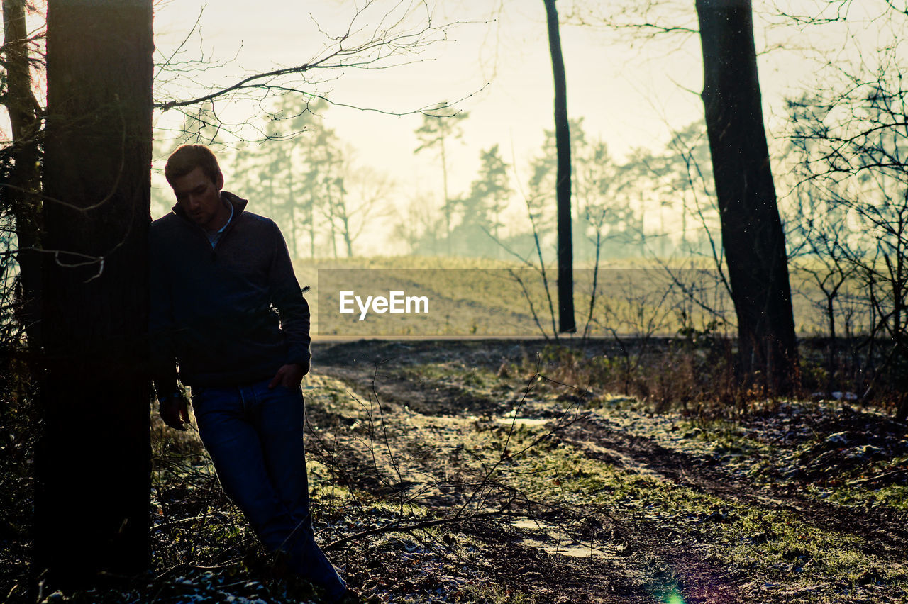 Sad man standing by tree at forest