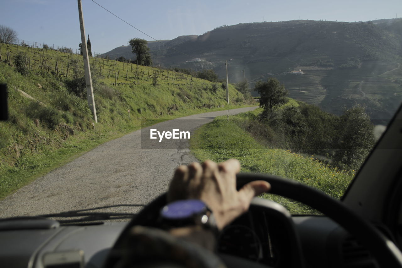 MAN DRIVING CAR ON ROAD AGAINST MOUNTAIN