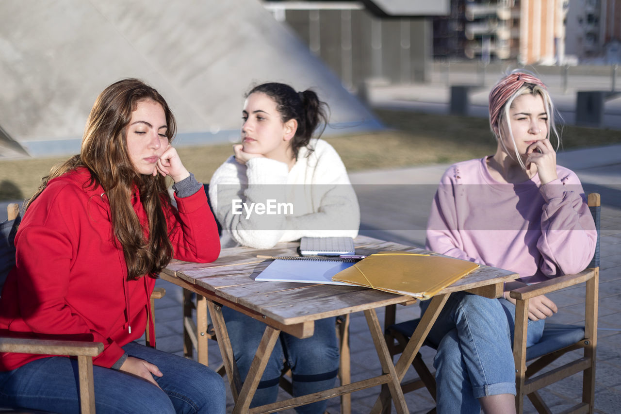 Young displeased women sitting by table outdoors