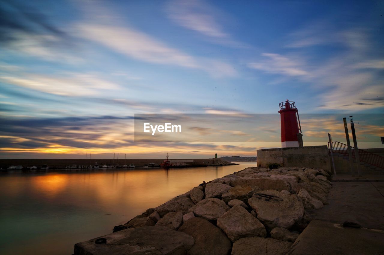 Lighthouse by building against sky during sunset