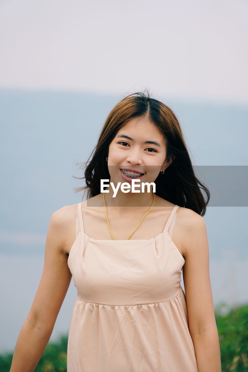 Portrait of a smiling young woman standing against sea