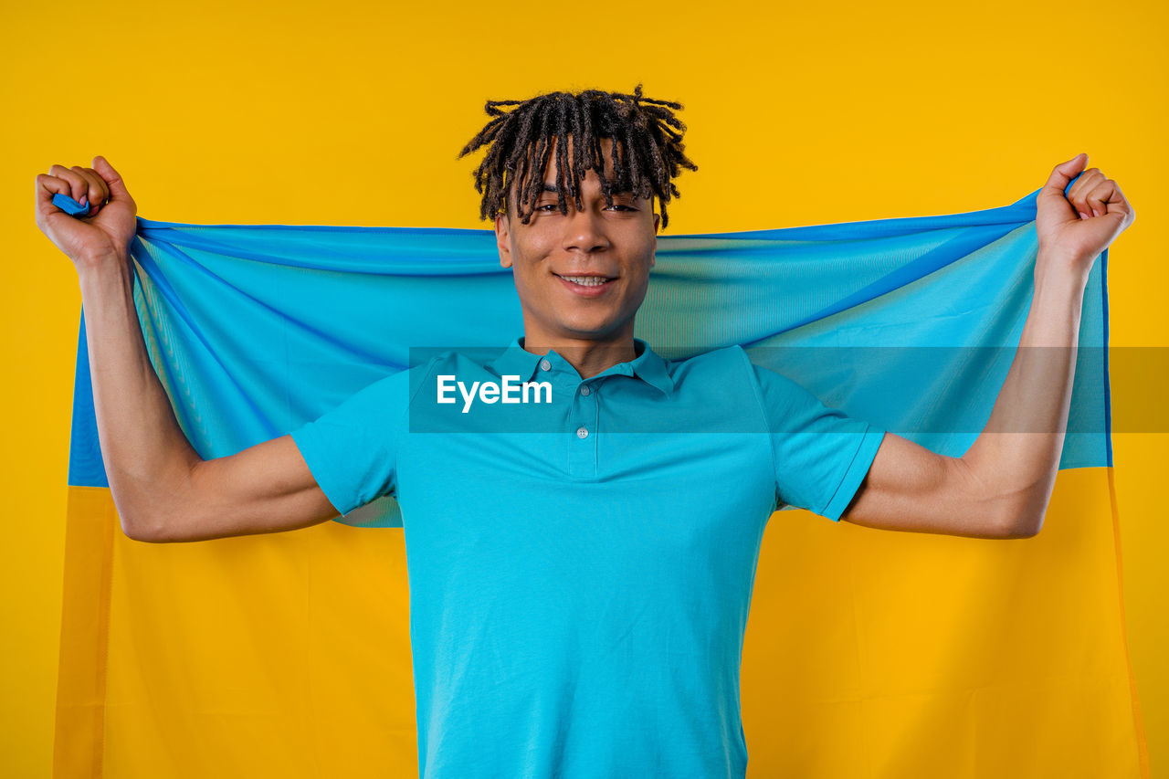 yellow, one person, studio shot, smiling, adult, colored background, happiness, emotion, blue, portrait, front view, clothing, standing, men, looking at camera, indoors, cheerful, fun, young adult, waist up, polo shirt, yellow background, lifestyles, arm, casual clothing, active shirt