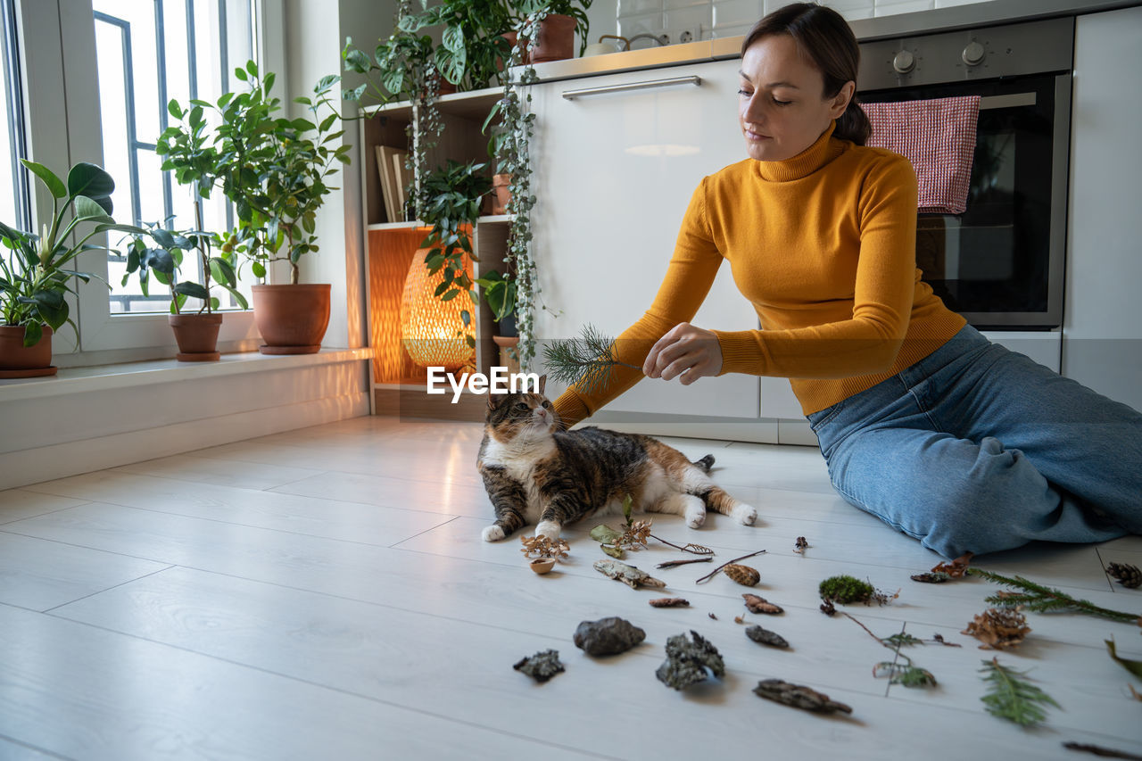Caring woman sitting on floor with cat, giving twig to sniff to prevent domestic pet dementia