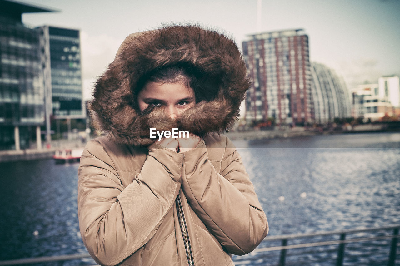 Portrait of young woman in warm clothing standing at riverbank