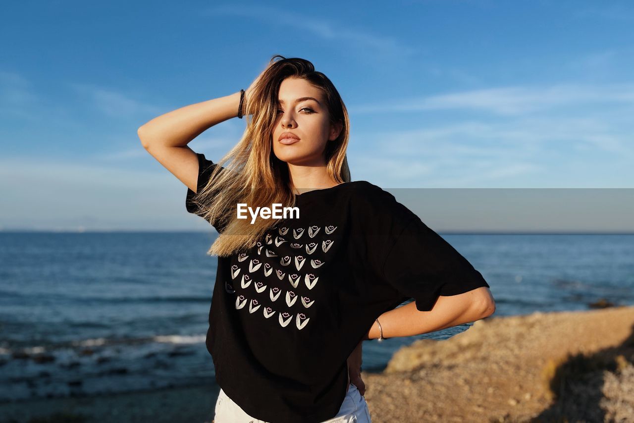 Young woman standing at beach against sky