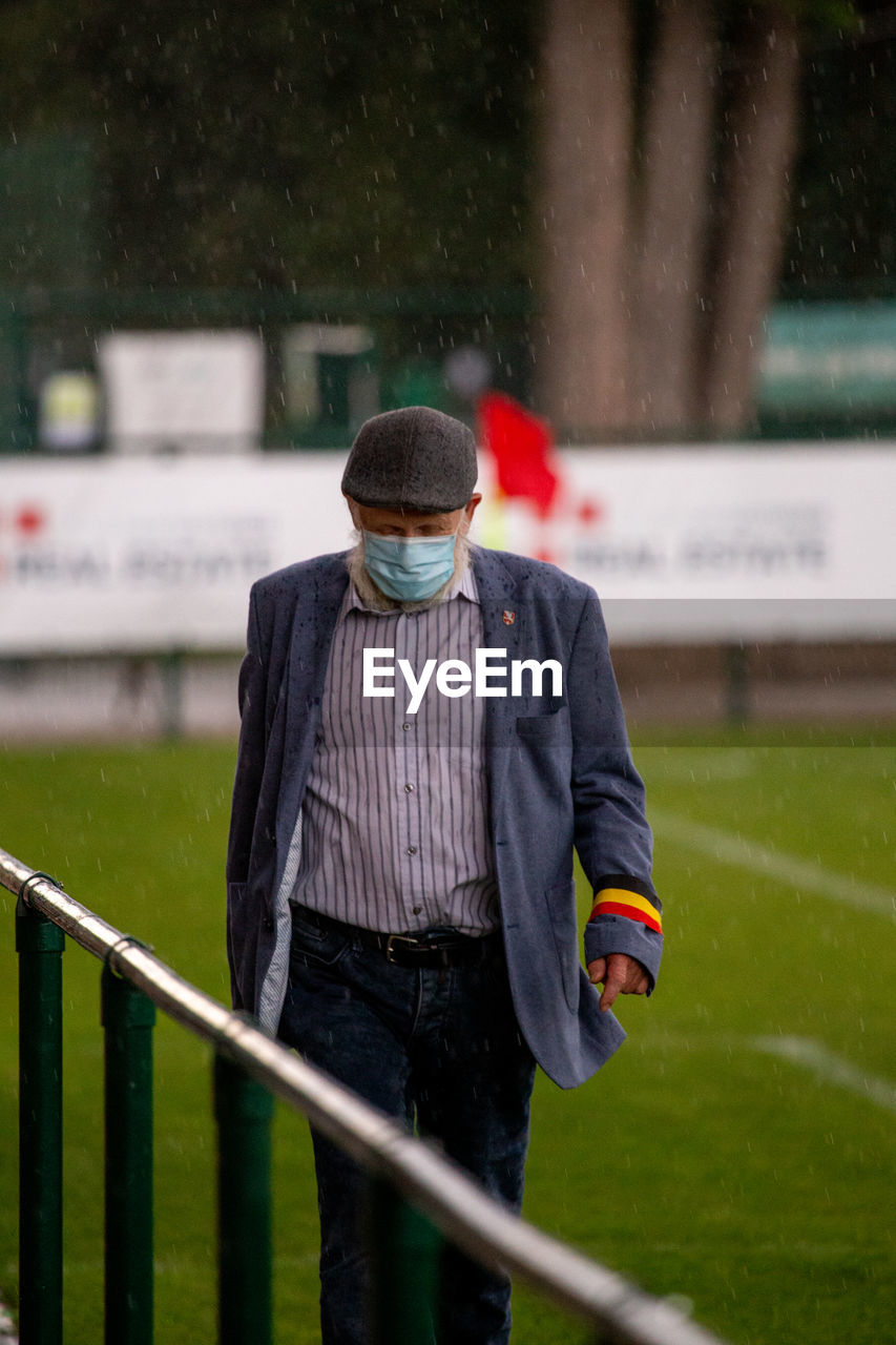 Man walking away from the soccer field in the rain wearing a mouth mask