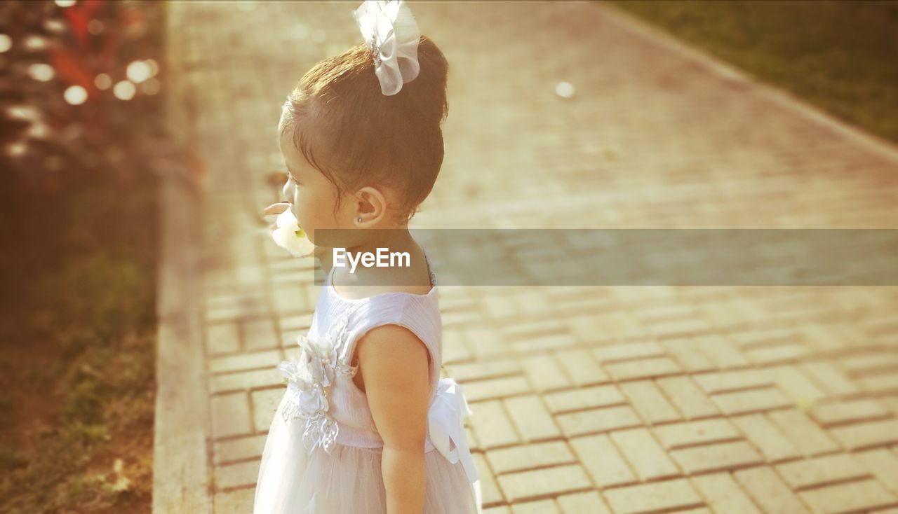 Side view of cute girl holding flower while standing on footpath