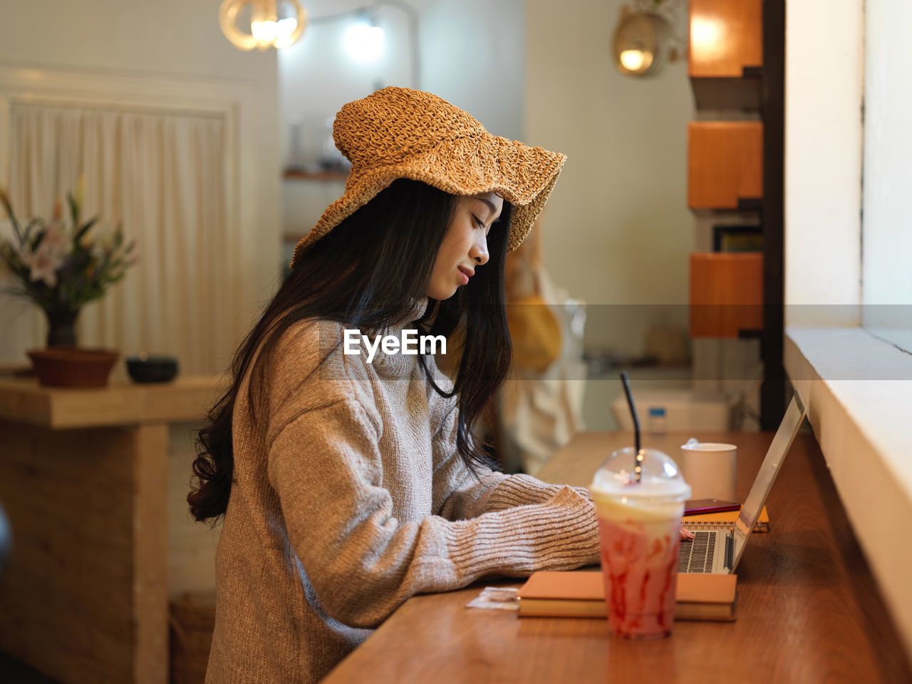 Young woman working on laptop by milkshake at cafe