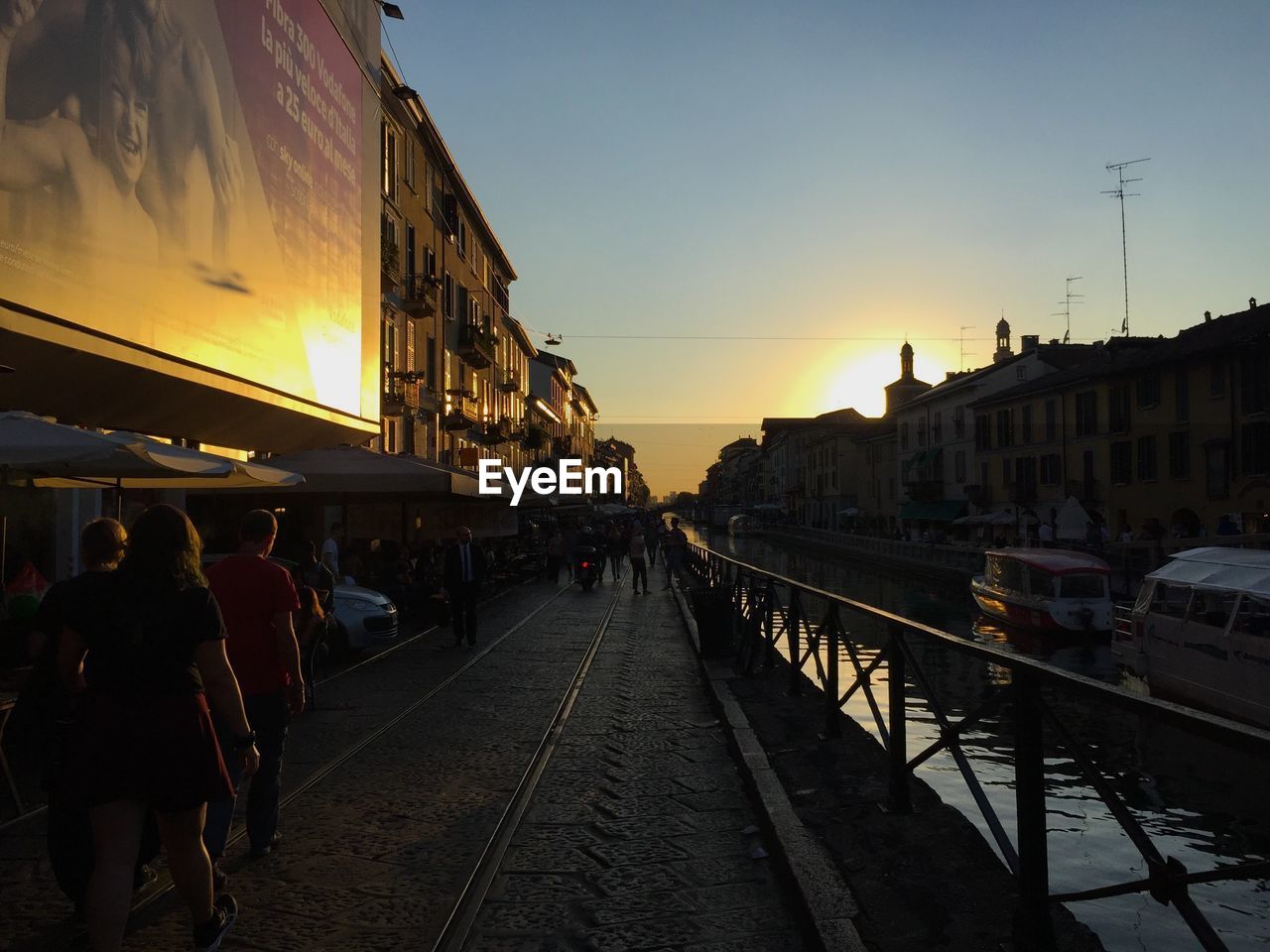 PEOPLE ON RAILROAD TRACKS IN CITY AGAINST SKY AT SUNSET