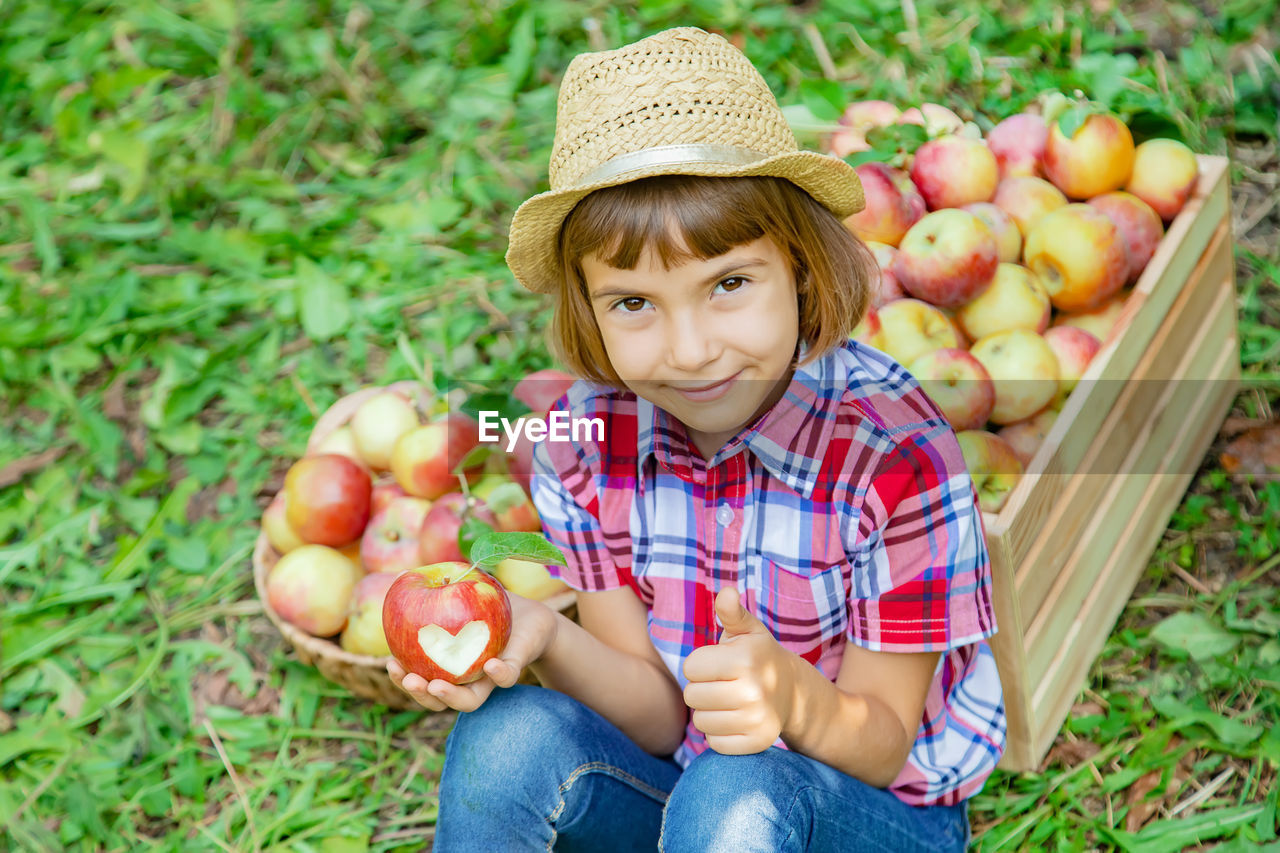 Portrait of girl holding apple sitting against crate