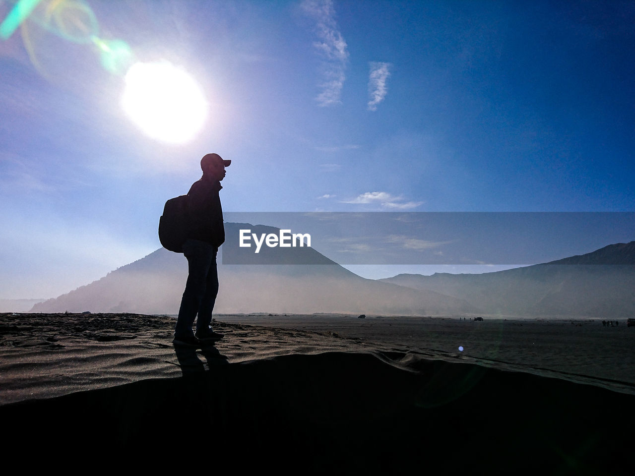 Side view of silhouette man standing on land against sky during sunny day