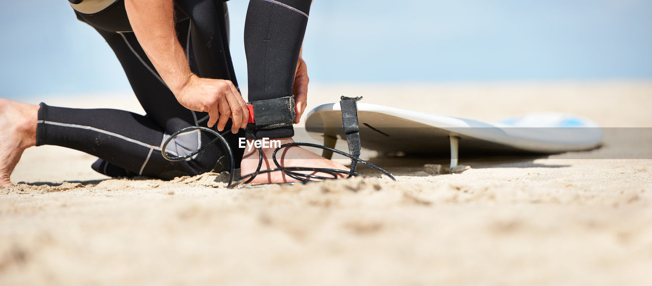 low section of woman tying shoelace at beach