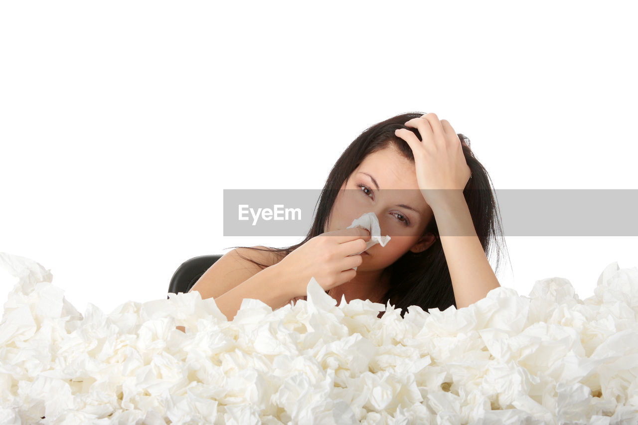 Portrait of woman with heap of facial tissues on desk against white background