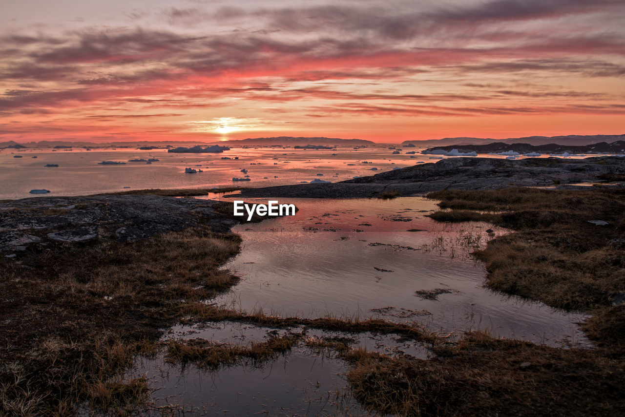 Scenic view of sea against cloudy sky at sunset