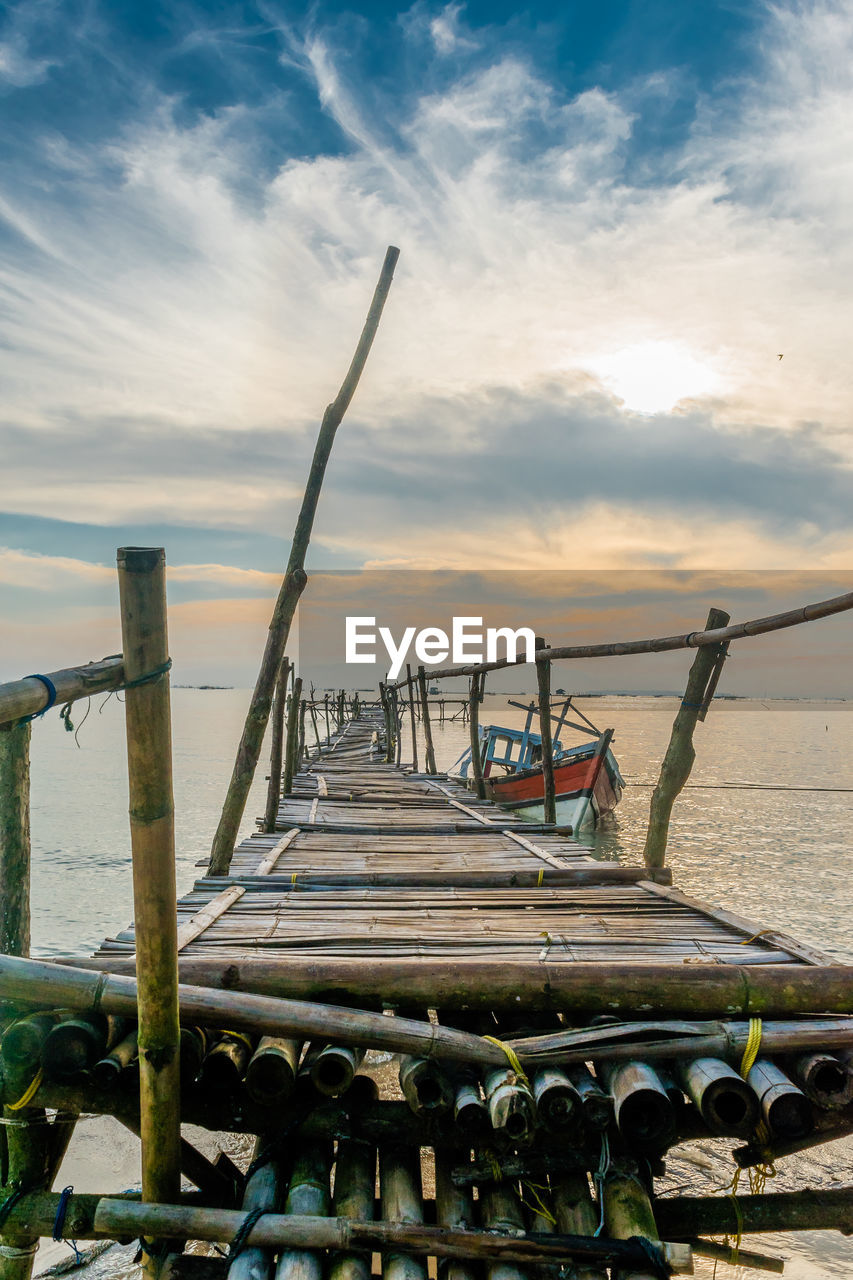 Wooden pier on sea against cloudy sky during sunset