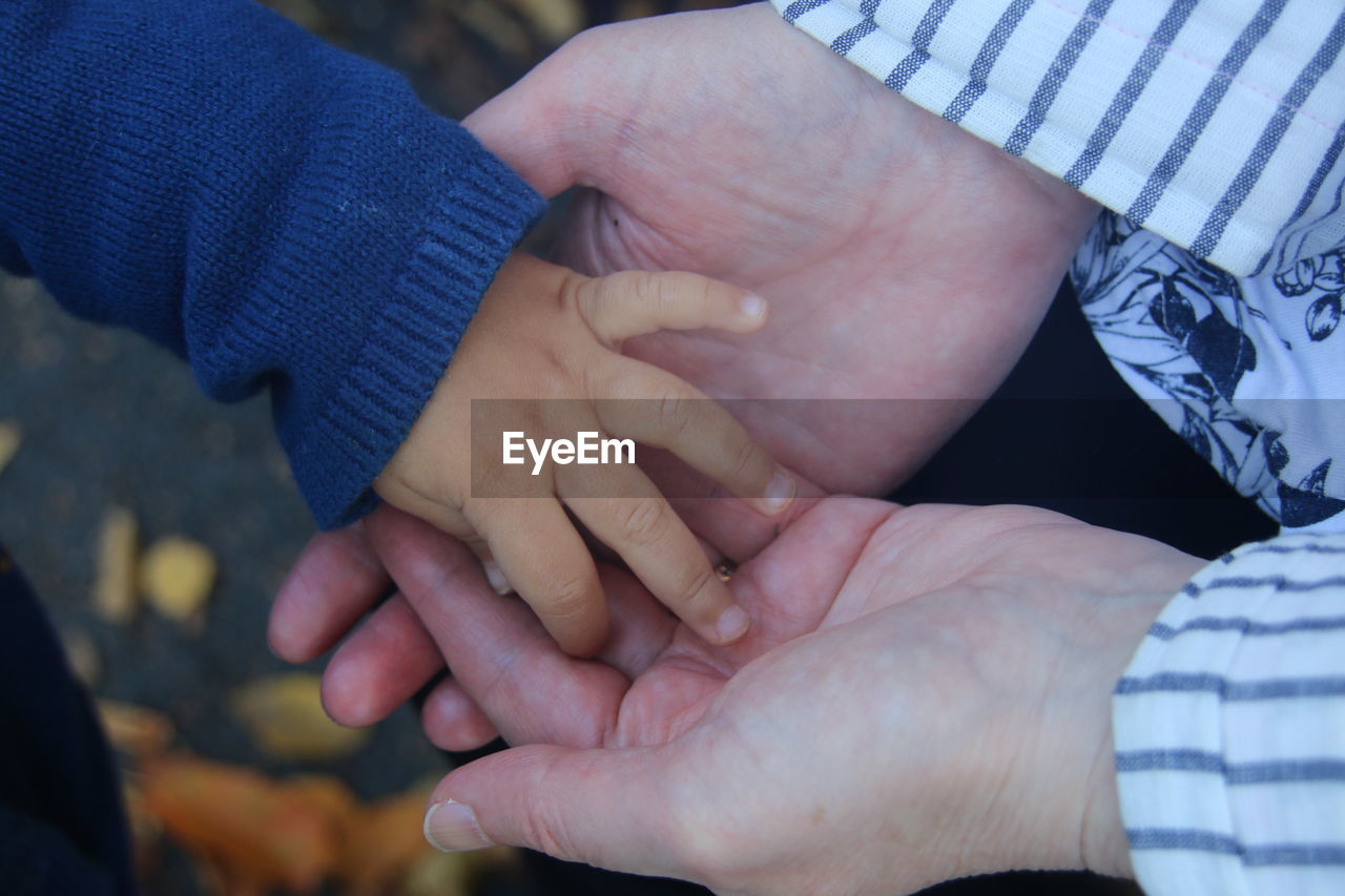 CLOSE-UP OF COUPLE HOLDING HANDS AND BABY