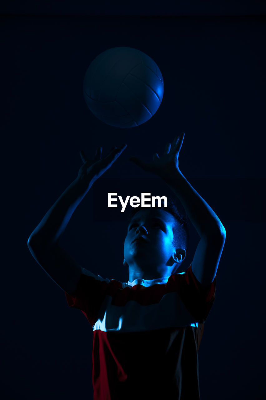 Close-up of boy holding volleyball against black background