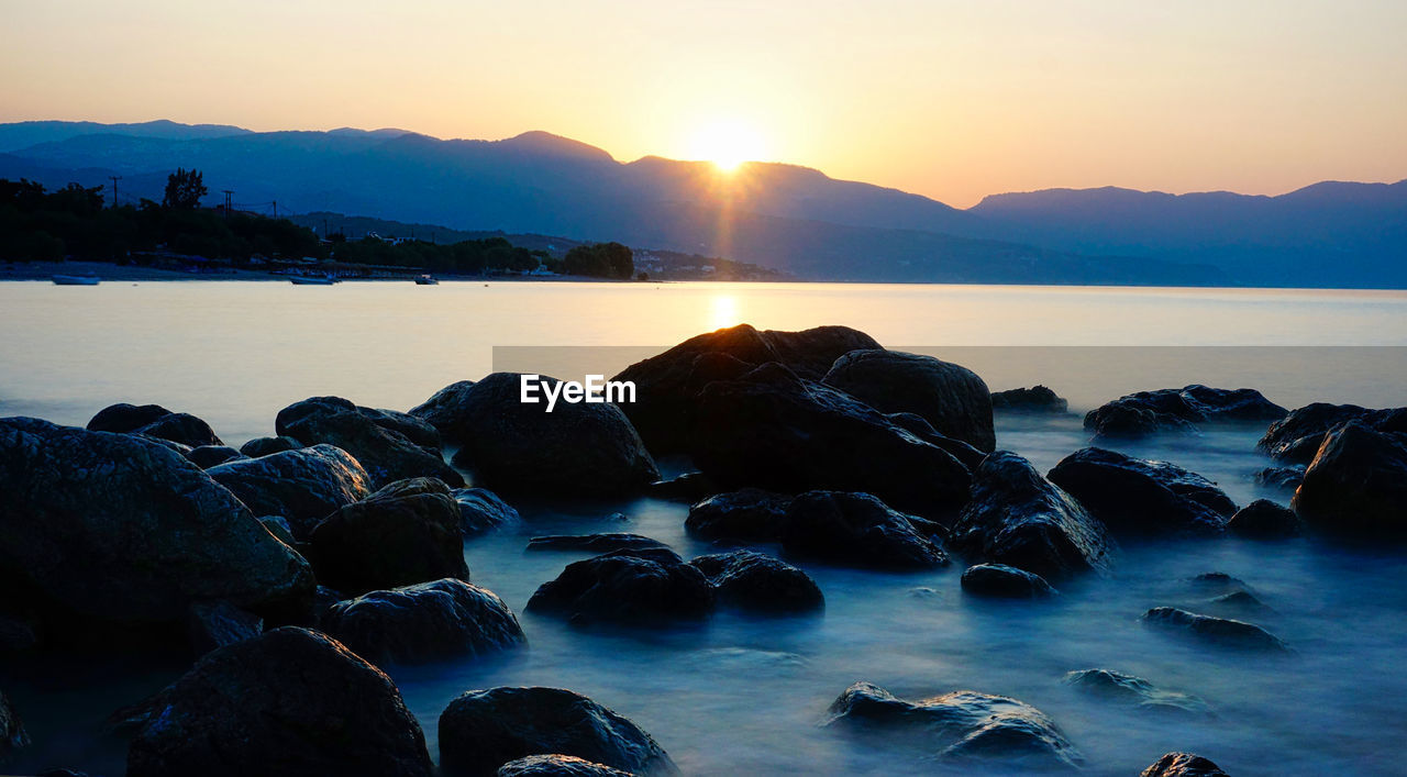 Rocks on sea shore against sky during sunset