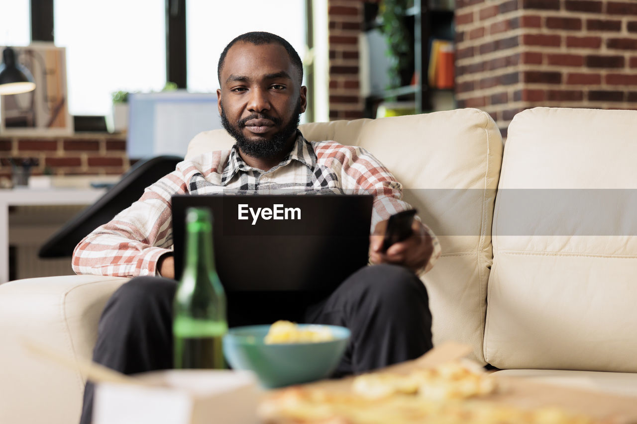 portrait of young woman using digital tablet while sitting on sofa at home