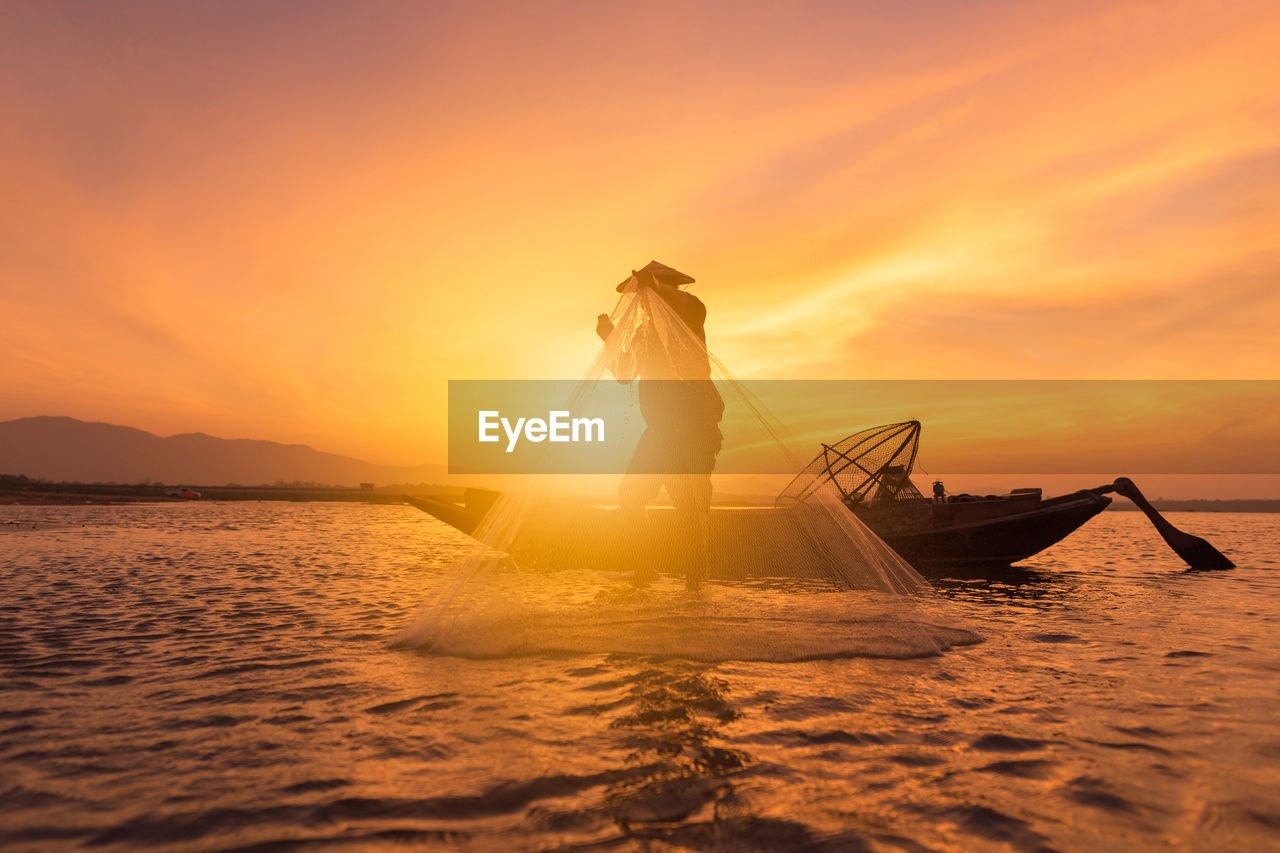 Man fishing in sea against orange sky