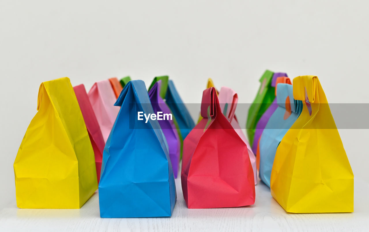 multi colored, studio shot, group of objects, yellow, variation, white background, no people, indoors, shopping bag, origami paper, cut out, copy space, in a row, vibrant color, group, large group of objects, bag, blue, consumerism, shopping, paper, retail