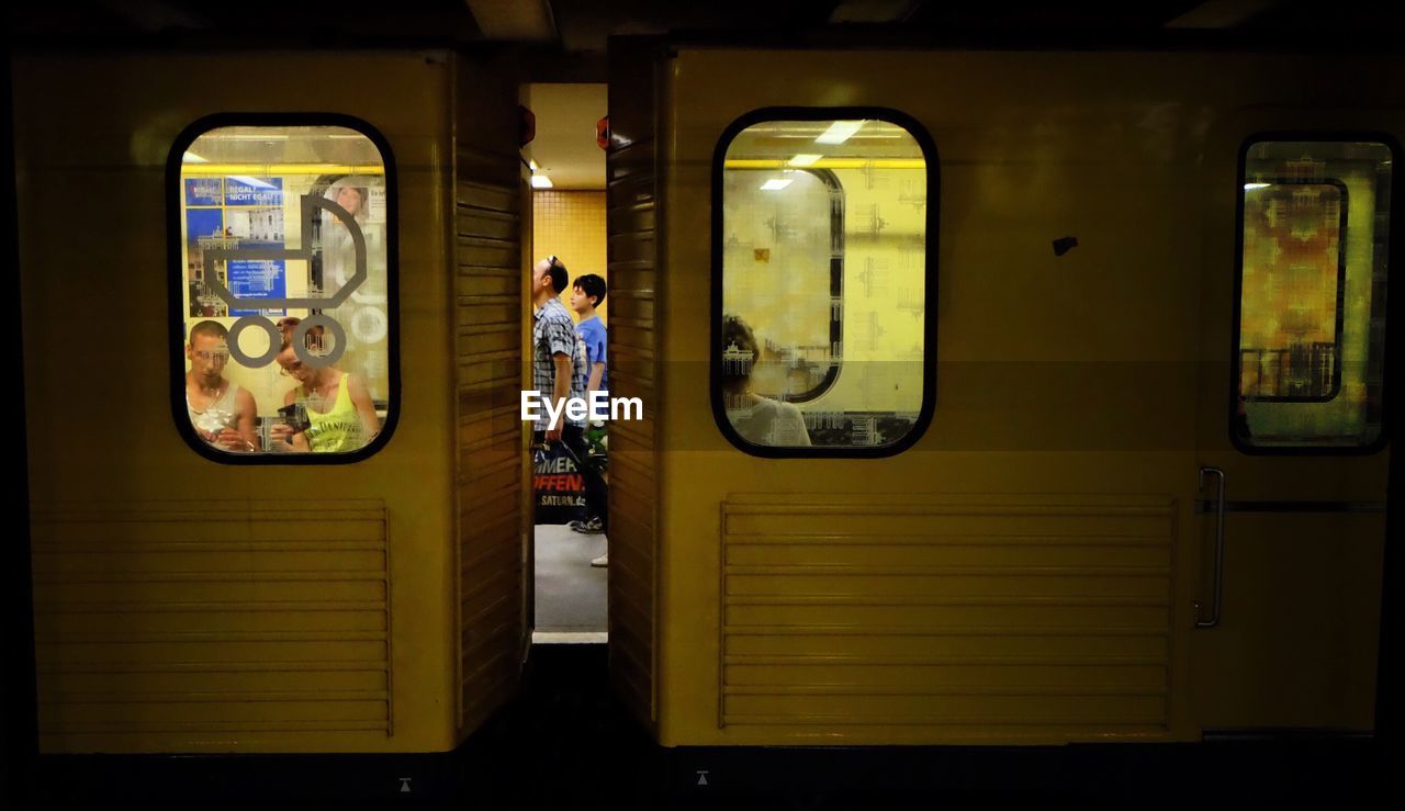 two people, real people, public transportation, men, standing, train - vehicle, transportation, night, mode of transport, women, railroad station platform, illuminated, lifestyles, rail transportation, full length, indoors, togetherness, adult, people