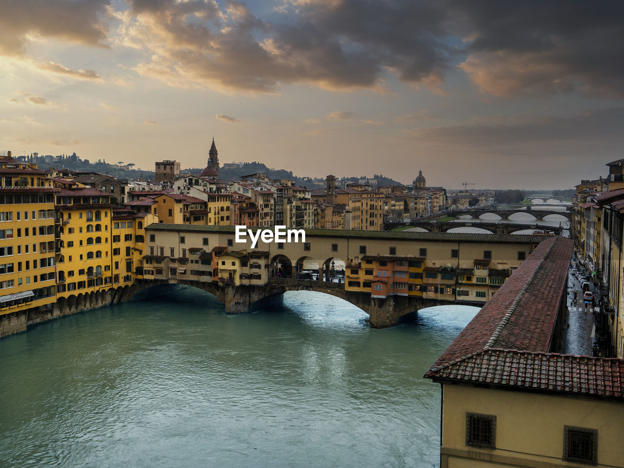 Arch bridge over river amidst buildings in city against sky