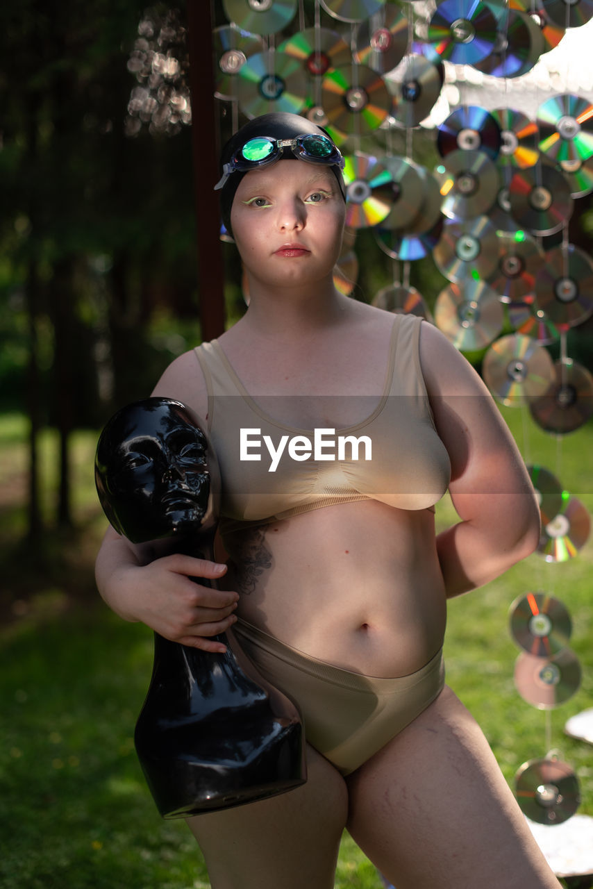 Portrait of young woman in a cap against the background of cd disks holds a mannequin in her hands