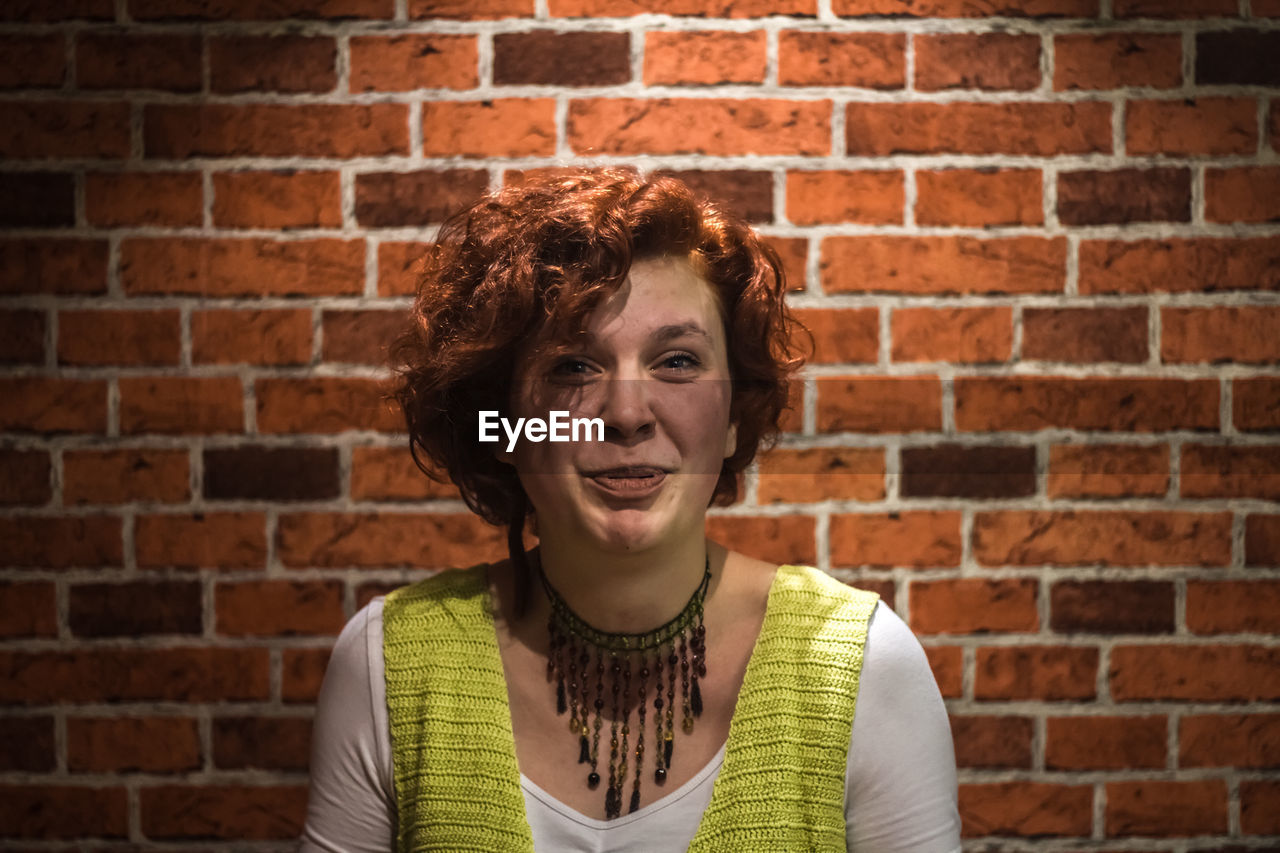 Portrait of smiling young woman against brick wall