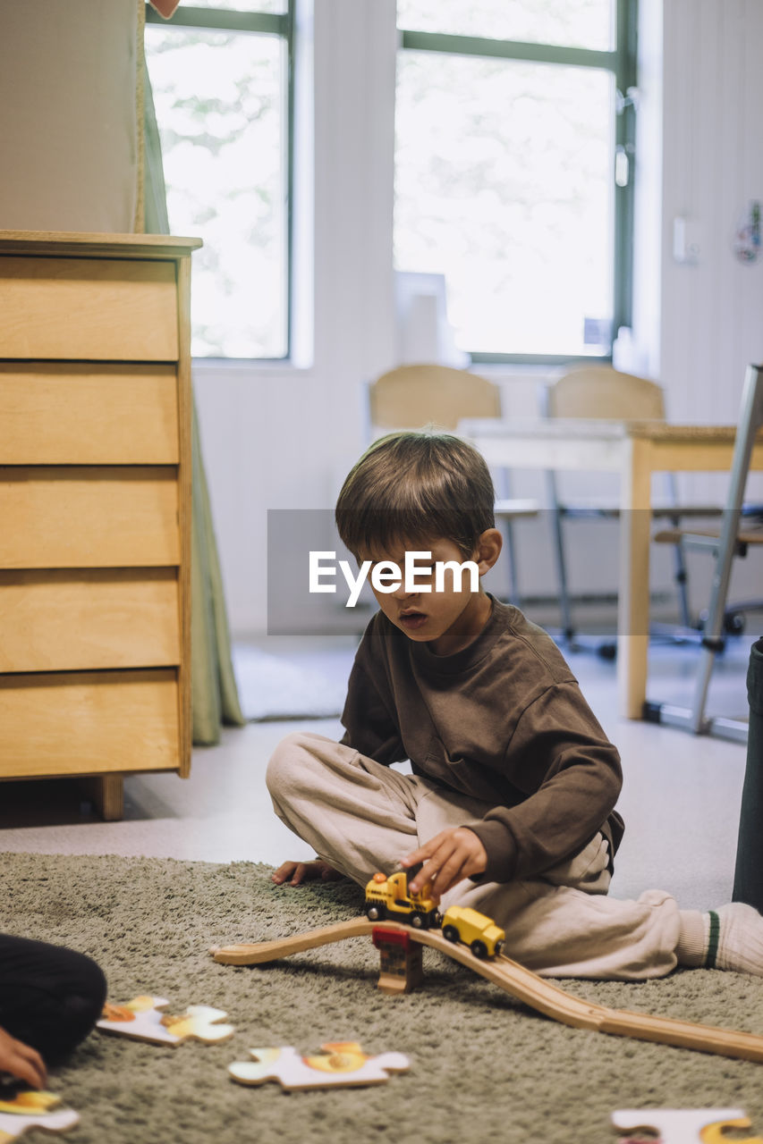 Boy playing with toy train while sitting on carpet in kindergarten