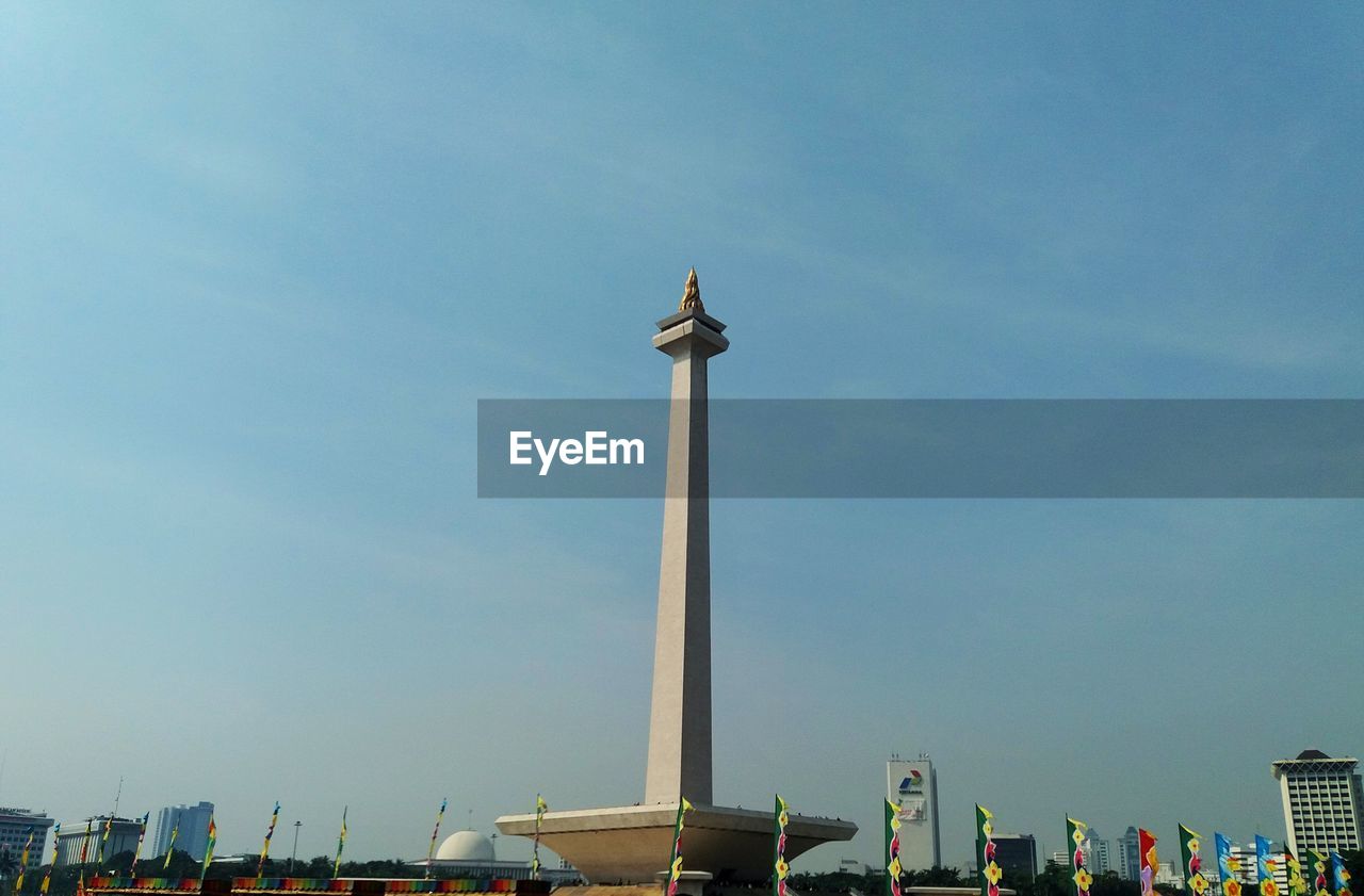 Low angle view of tower and flags against blue sky