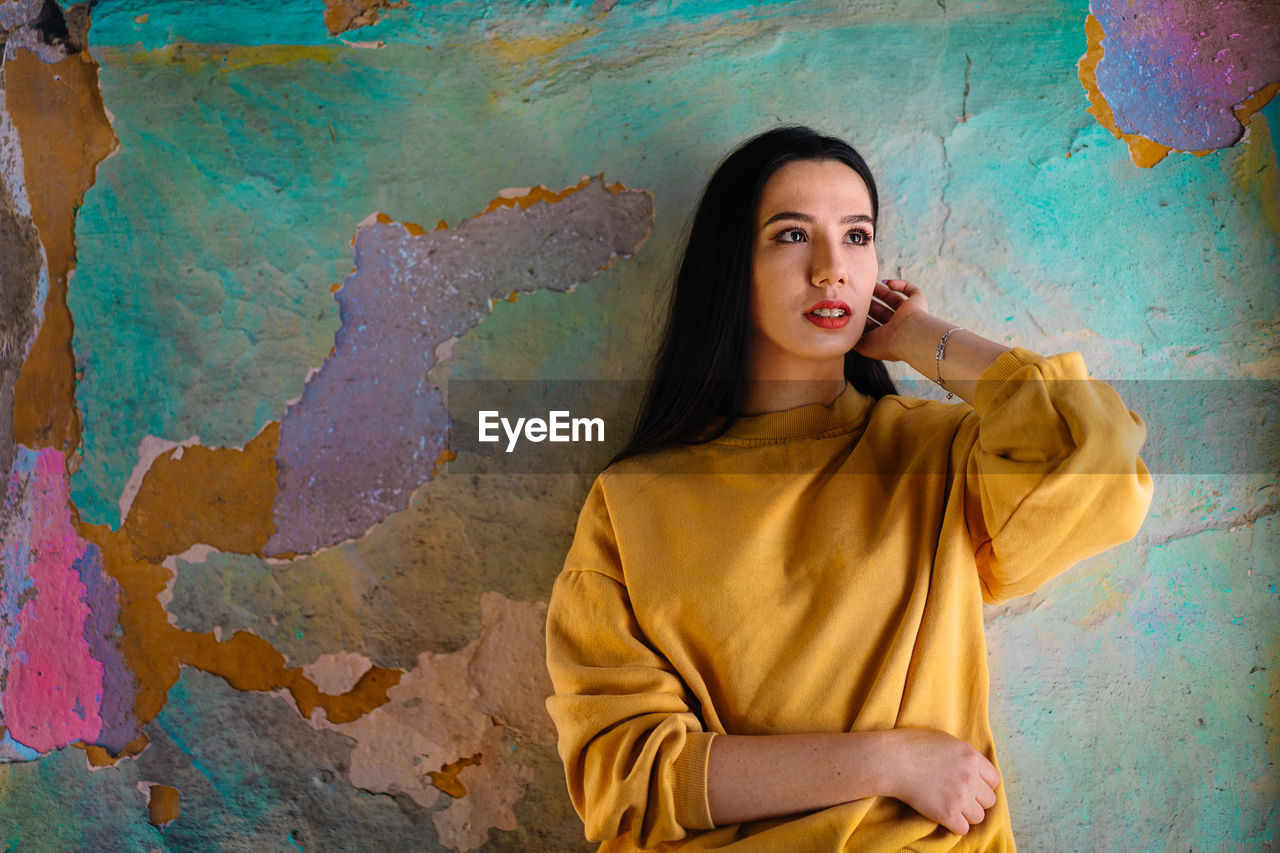 Portrait of beautiful young woman standing against colorful wall