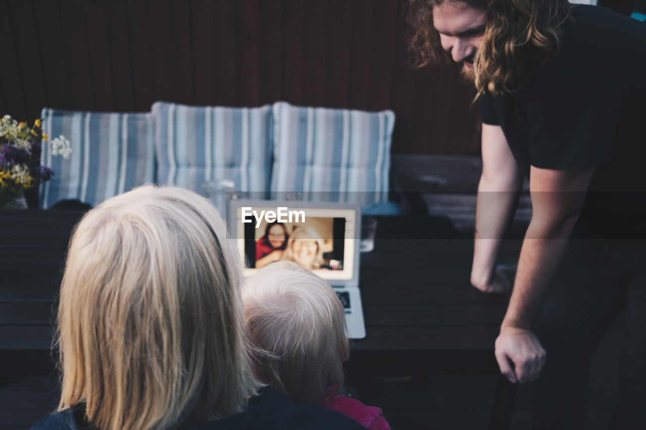 Man looking at mother and daughter doing video conference on laptop in holiday villa