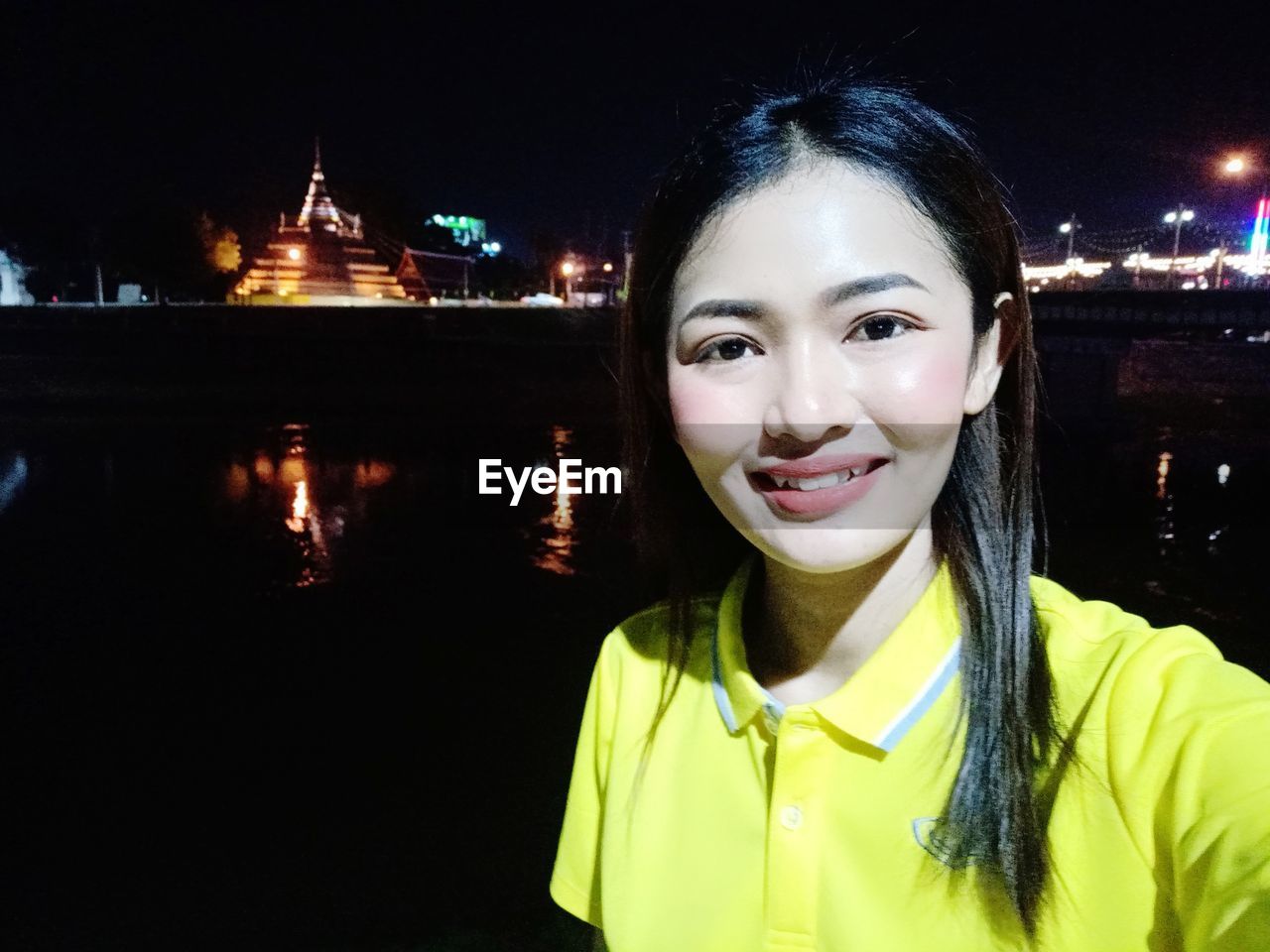 PORTRAIT OF SMILING YOUNG WOMAN IN ILLUMINATED WATER AT NIGHT