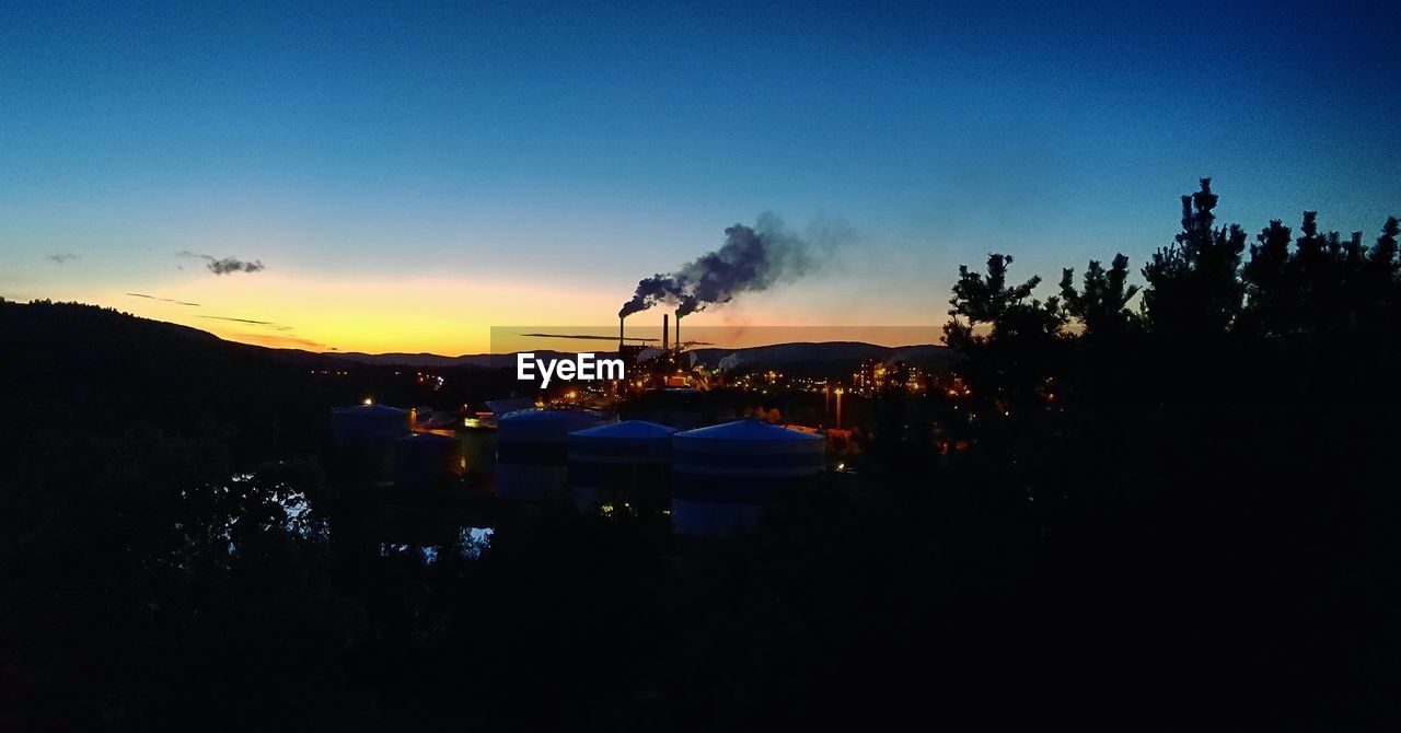 SILHOUETTE OF BUILDINGS AND TREES AGAINST SKY DURING SUNSET