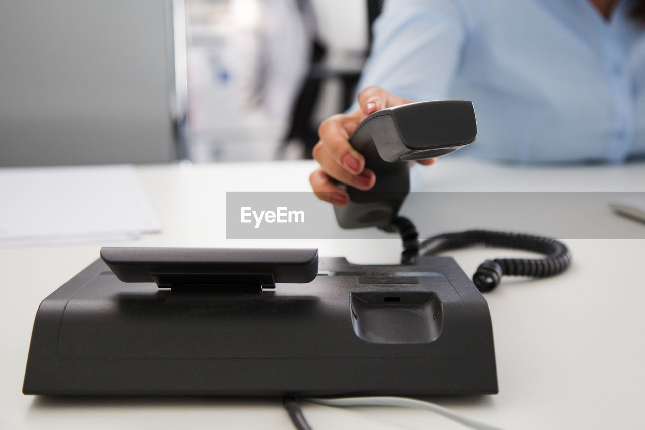 Midsection of woman holding telephone at desk in office