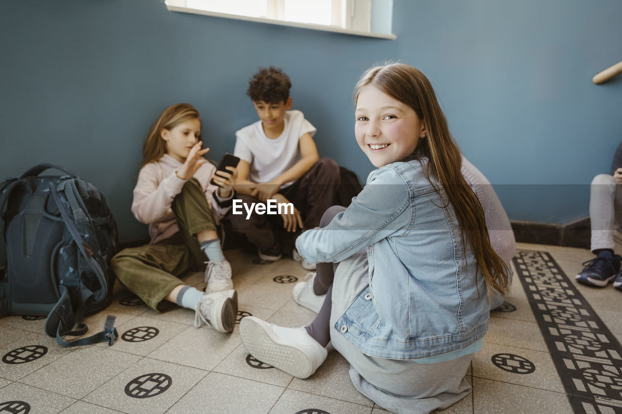 Portrait of smiling girl sitting on floor with friends in school