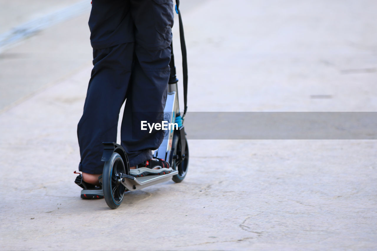 Low section of man riding push scooter on road