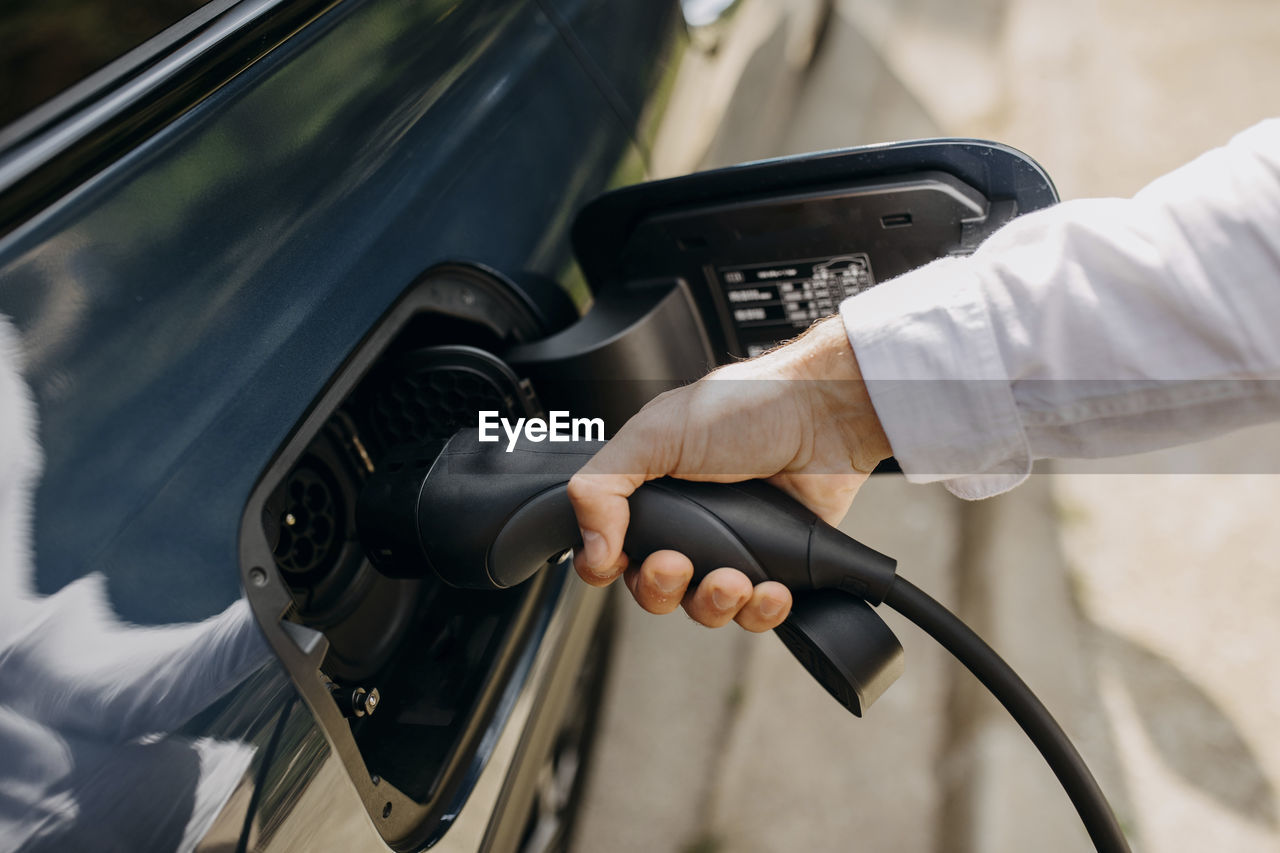 Man holding electric plug of hybrid car at charging point