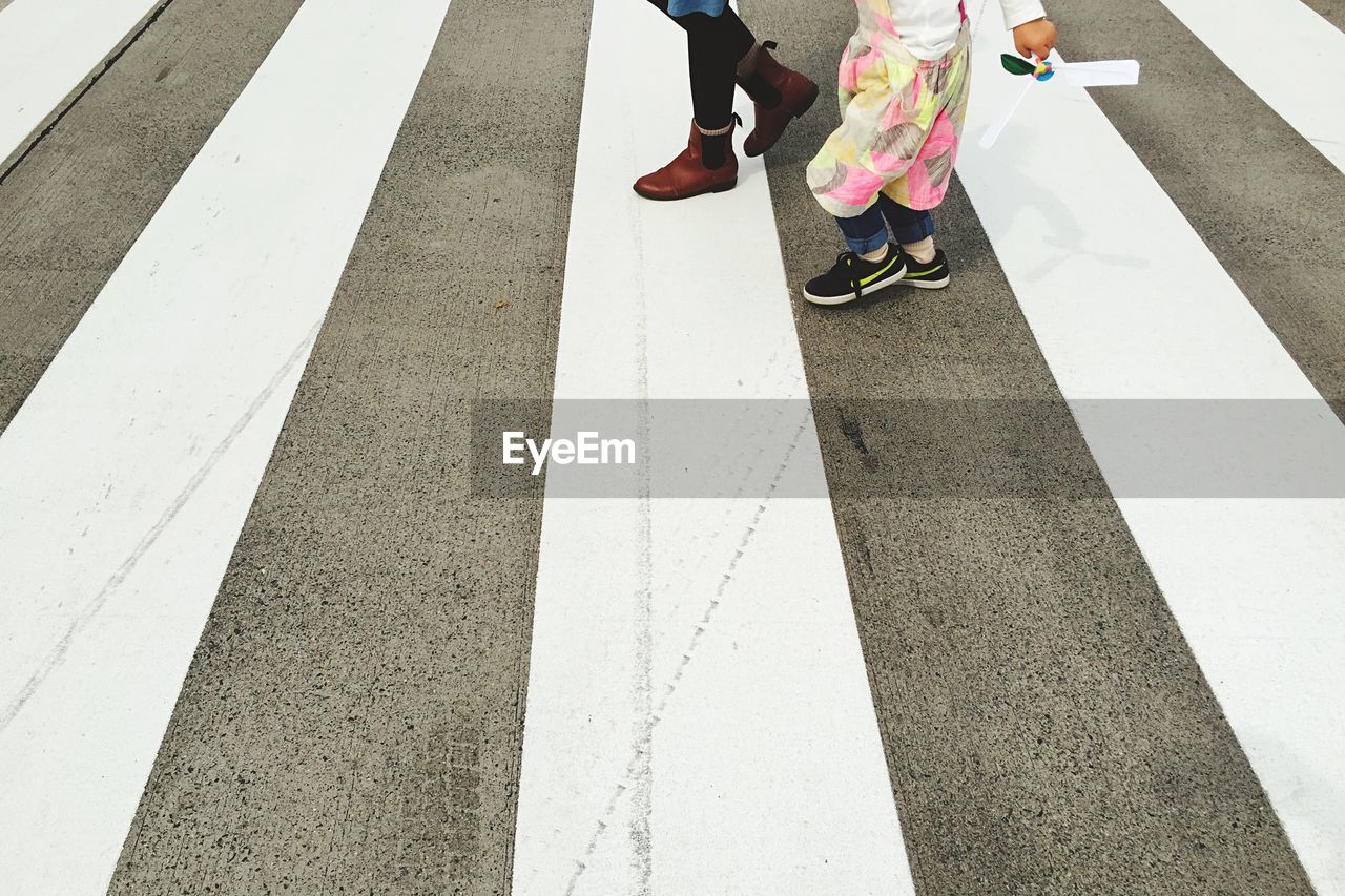 Low section of woman and girl walking on zebra crossing