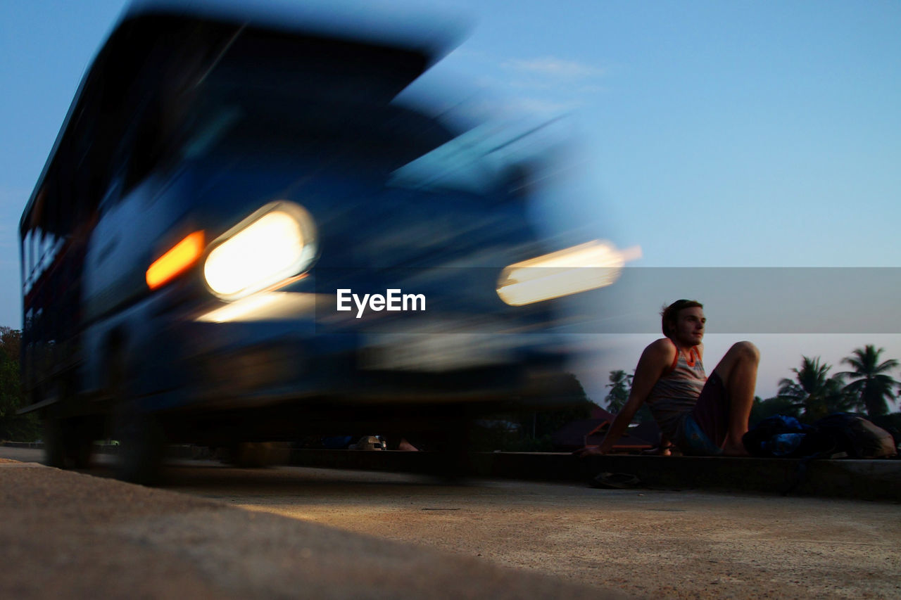 Blurred motion of vehicle moving on road by man during sunset