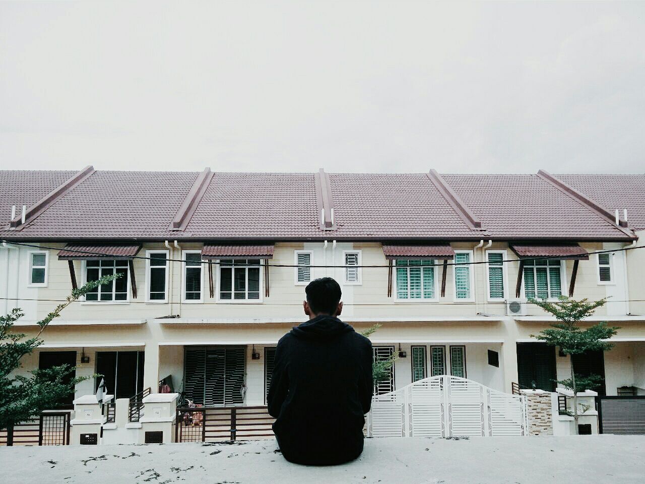 Man sitting in front of house against clear sky