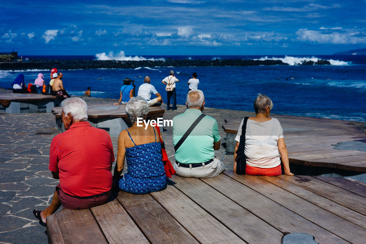 Rear view of senior people sitting on wooden table by sea