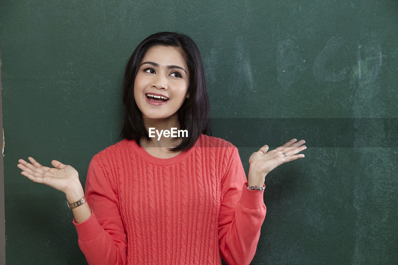 Cheerful female teacher gesturing while standing by blackboard